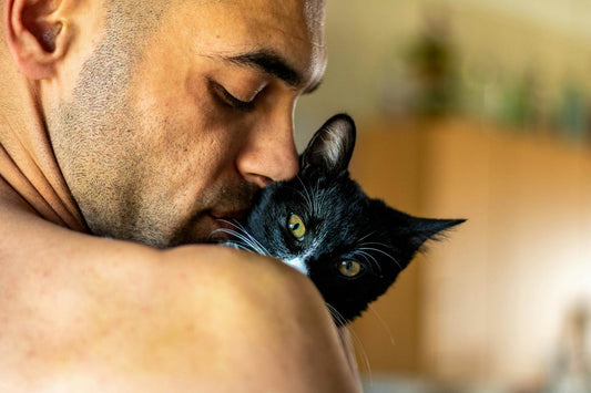 A man warmly holds his black and white cat in a cozy home setting